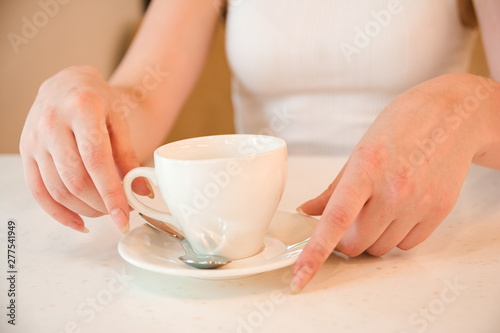 Holds cup with drink in his hands on table