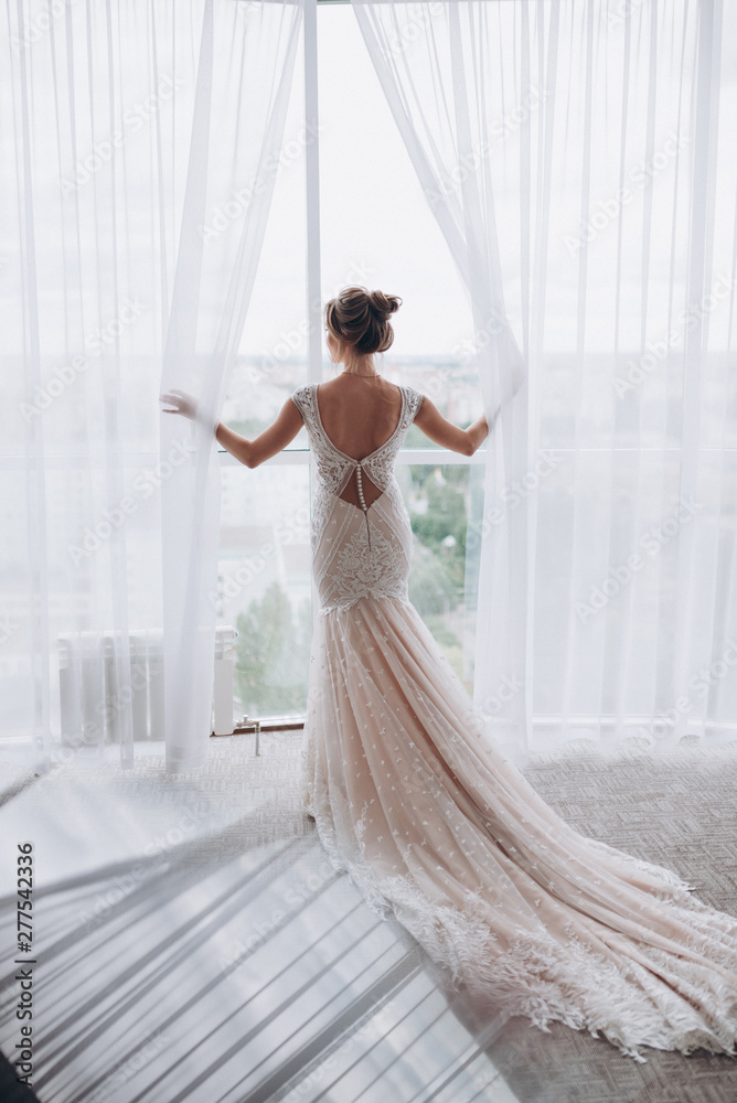 the bride in the dress stands at the large panoramic window the bride in the dress stands at the large panoramic window