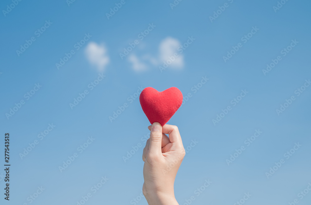 Woman hand holding a red heart with a bright blue background. Love concept