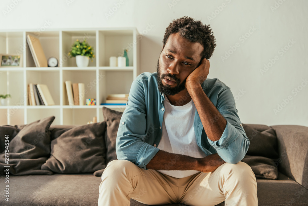 thoughtful african american businessman sitting on couch at home and suffering from summer heat