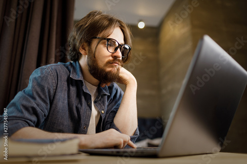 Student bearded man studying with laptop, indoors appartment view