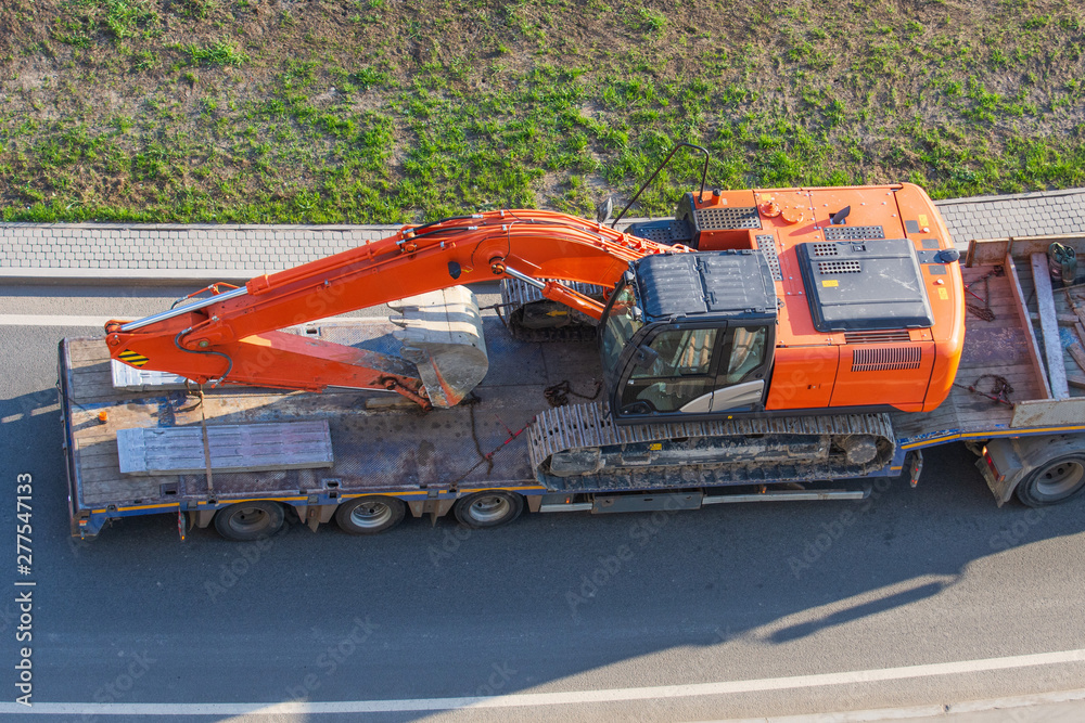 Truck with a long trailer platform for transporting heavy machinery, loaded excavator. Highway transportation.