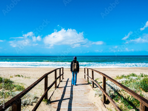 an Italian woman shot from behind feels free while walking along a wooden path towards the sea, on the beach in early spring in the nature
