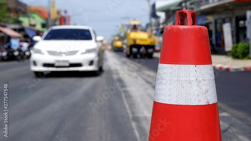 Focus on traffic cone and blurred background of road rollers laying of new asphalt and transport zone demarcation on the street in the city, construction concept