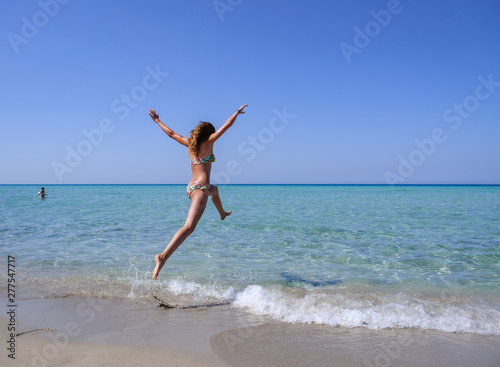 Slim and athletic girl in a colourful bikini jumping into the crystal clear water of a beautiful beach -vacation-fitness-wellness