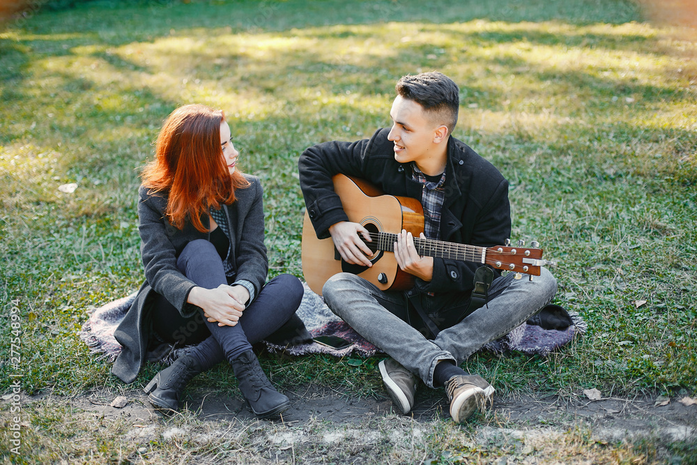 Cute couple in a park. Lady with red hair. Guy with a guitar Cute couple in a park. Lady with red hair. Guy with a guitar