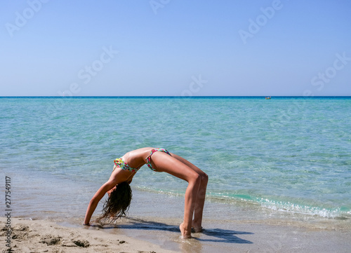 Slim and athletic girl doing yoga, calisthenics, fitness training on a wonderful beach with crystal clear water -vacation-fitness-wellness