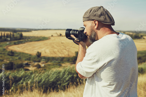 photographer with a camera stands on the background of cereal fields. a man wearing shorts and a t-shirt, a cap on his head