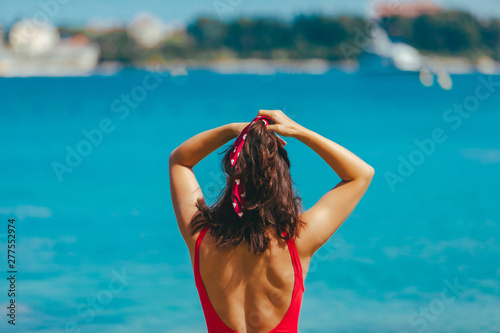 sexy woman in red swimsuit walking into blue clear sea water