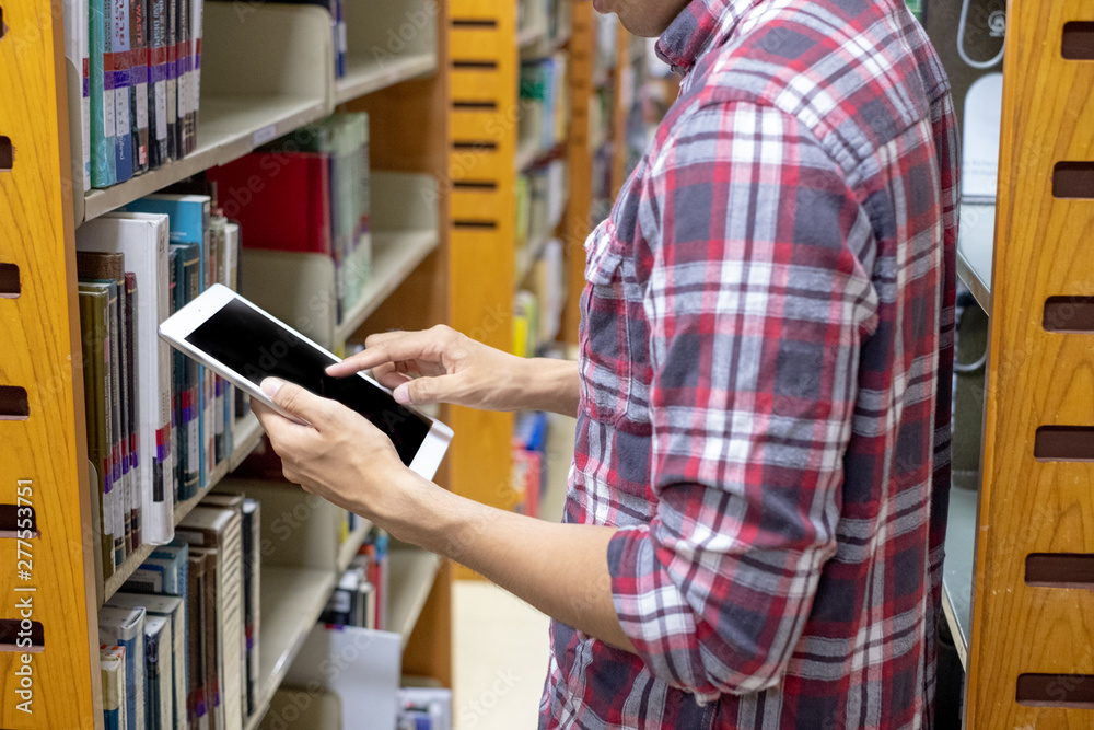 Male students use technology to find books to read in the library. Education concept Male students use technology to find books to read in the library. Education concept