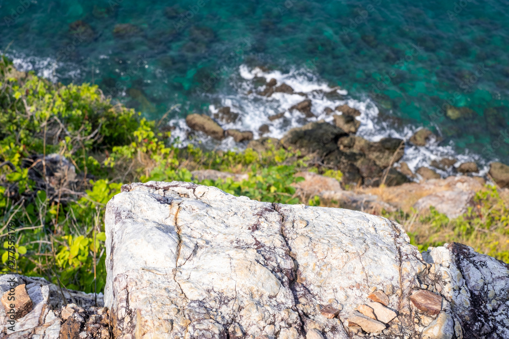 Looking over a cliff edge with blue sea below and Cliff edge and the sea. Stones worn smooth along the top of a cliff and a blue sea below.