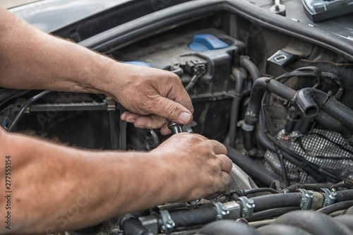 Two hands carry out repairs in the engine compartment of a car..
