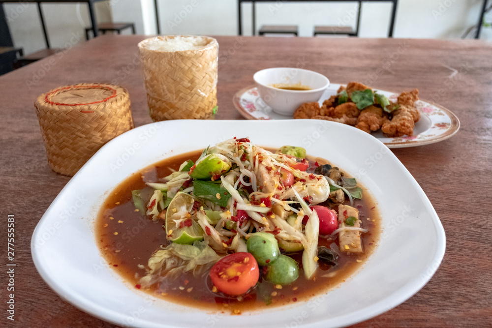green papaya salad in White plate and sticky rice on wooden background. green papaya salad in White plate and sticky rice on wooden background.