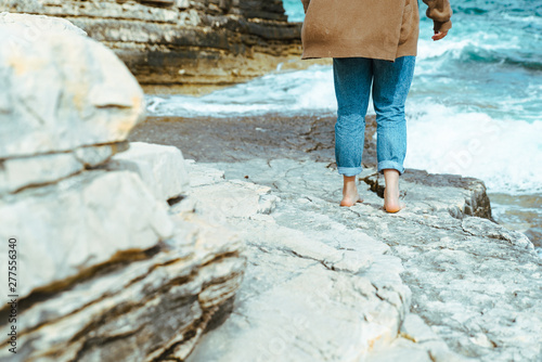 woman walking by rocky sea beach at sunny windy day. summer vacation