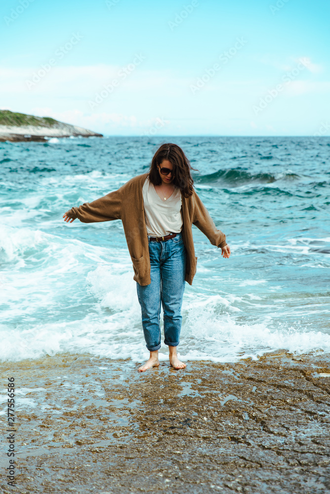 woman walking by rocky sea beach at sunny windy day. summer vacation
