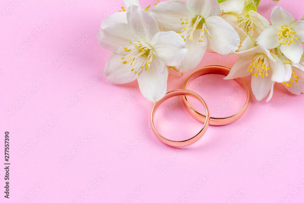 pair of gold wedding rings and white Jasmine flowers on pink background with copy space pair of gold wedding rings and white Jasmine flowers on pink background with copy space