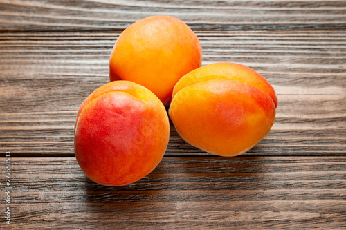 Ruddy apricots on a wooden background. Top view of three fresh juicy apricots piled on a wooden table.
