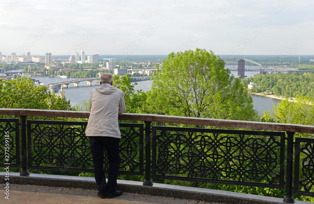 A man leaning on the railing of the fence, admiring the view of Kiev and the Dnieper on Vladimirskaya Gorka