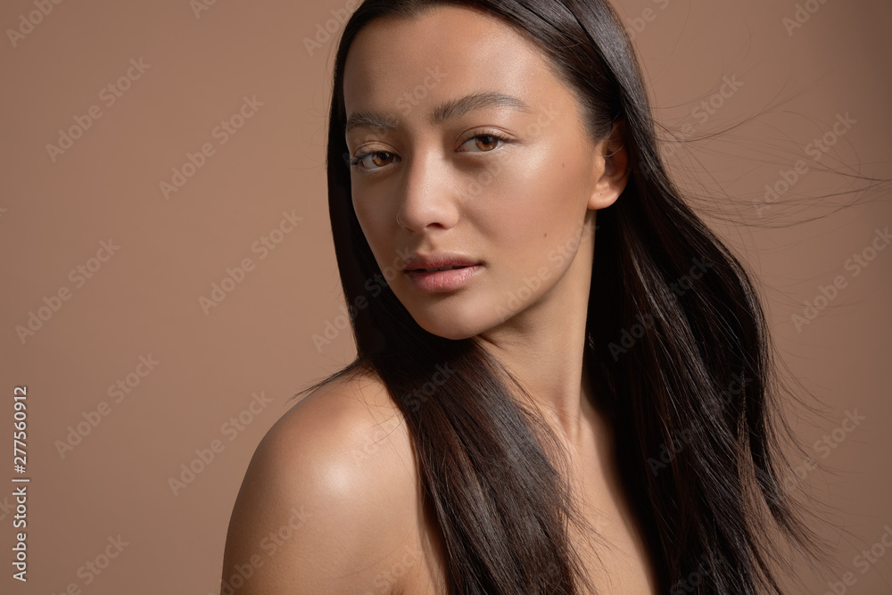 beauty brunette model mixed race model with long strong straight hair blowing. Ideal skin natural makeup on beige background beauty brunette model mixed race model with long strong straight hair blowing. Ideal skin natural makeup on beige background