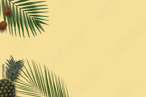 Top view yellow pineapple and kiwi flatlay. Summer minimal banner copyspace. Green palm leaves on the pastel background