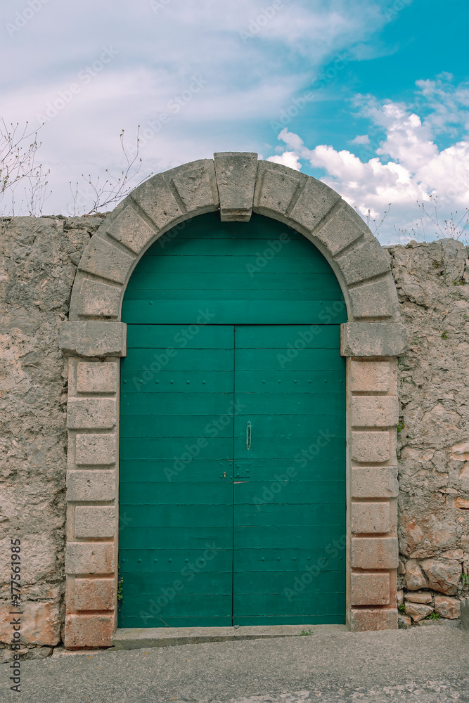 Green arched door in a stone fence against a blue sky Green arched door in a stone fence against a blue sky