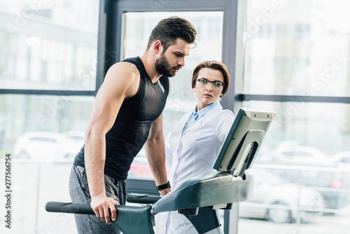 sportsman training on treadmill near doctor during endurance test in gym