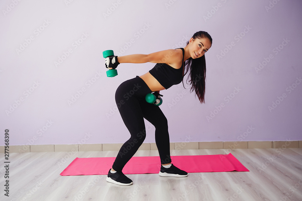 Stylish brunette in a black top. Woman spend time in a gym. Girl with green dumbbless Stylish brunette in a black top. Woman spend time in a gym. Girl with green dumbbless