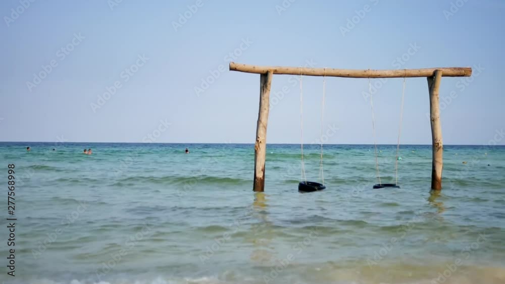 Beautiful sea landscape. High wooden swing decorated with colorful ribbons in a calm azure sea near the coastline. Beautiful sea landscape. High wooden swing decorated with colorful ribbons in a calm azure sea near the coastline.