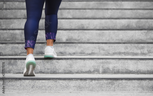 Female runner athlete doing a stairs climbing. Running woman doing run up steps on staircase in urban city. Doing cardio sport workout. Exercise outside in summer. Activewear leggings and shoes.