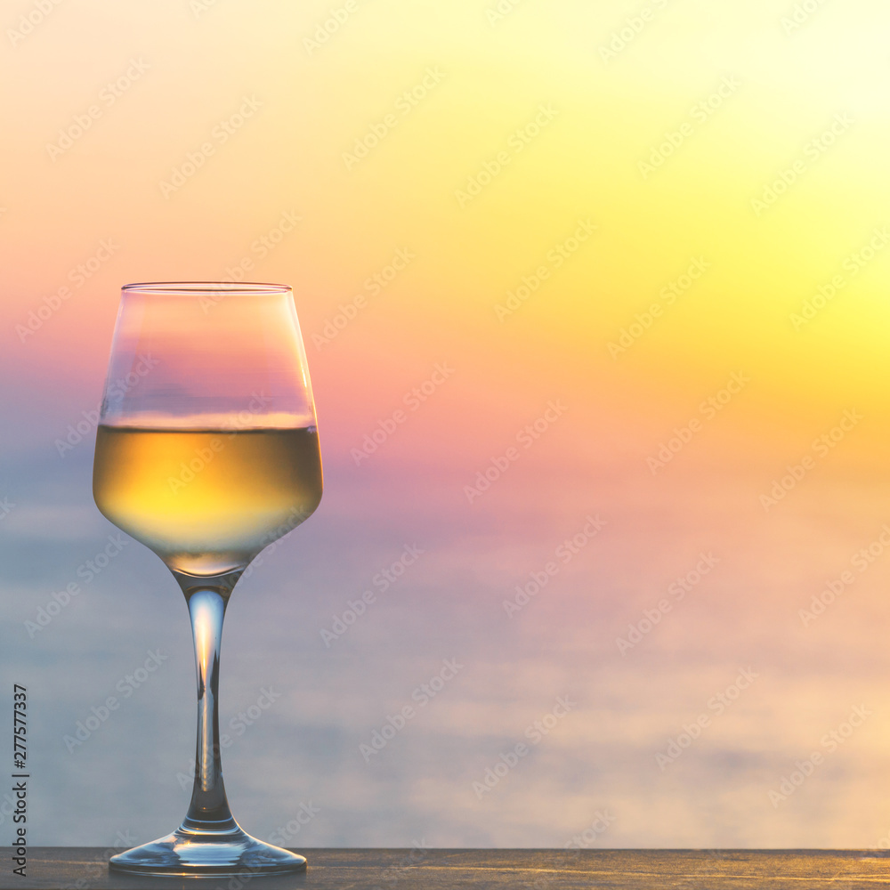 Glass of white wine against sunset. Beautiful summer evening sea view.