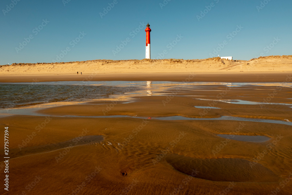 Sunset at low tide with red and white lighthouse on the beach