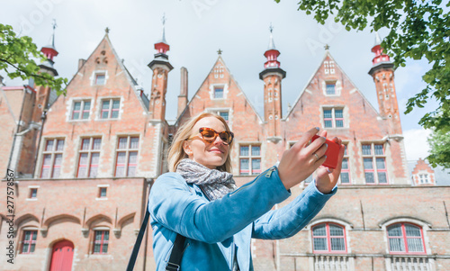 Stylish young female tourist takes a selfie on a mobile phone in Bruges, Belgium.
