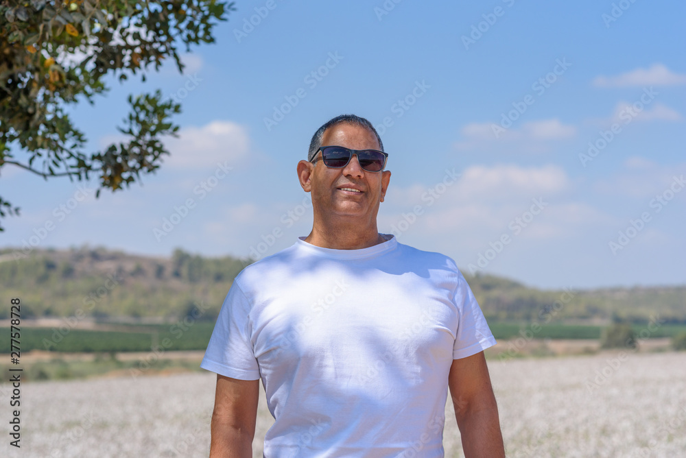 Portrait Of Handsome Senior Man In Outdoors. Sporty athletic elderly man on background of sky and cotton field. Senior farmer standing in meadow background.