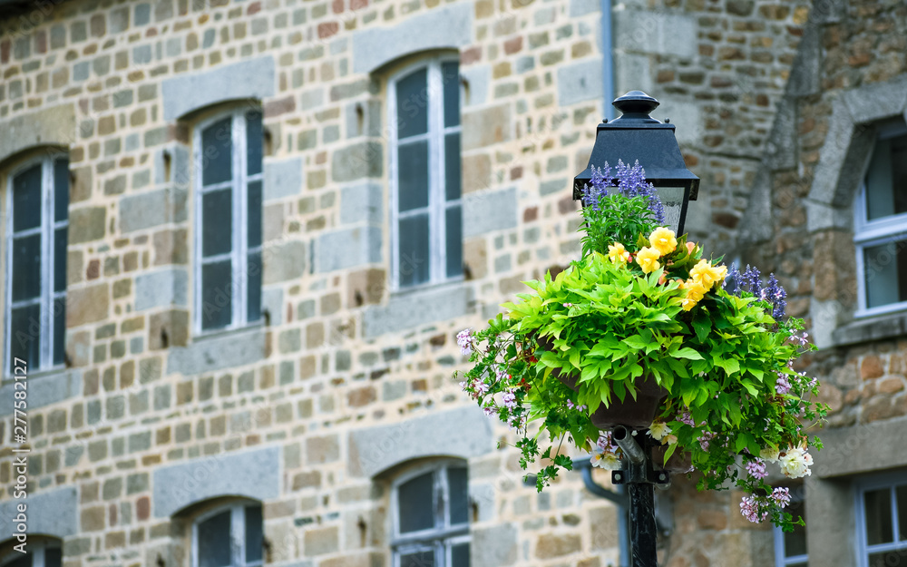 Lamppost adorned with flowers, with defocused background of typical house of the French brittany.