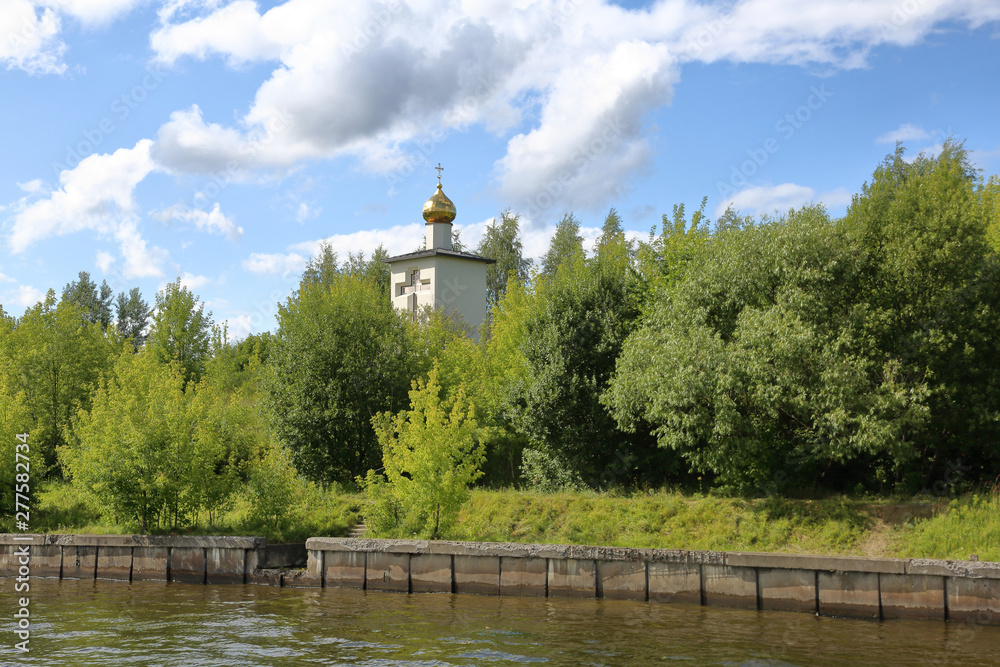 The golden dome of the white stone Orthodox church on the bank of the river