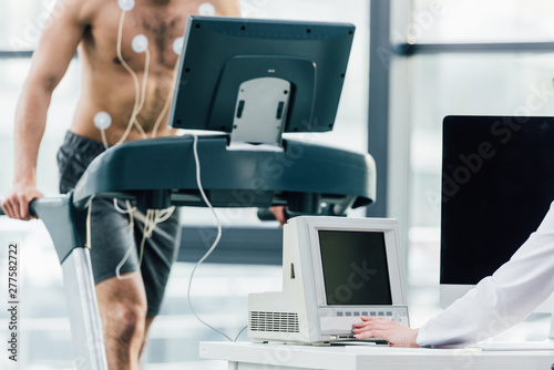 Fototapeta Naklejka Na Ścianę i Meble -  cropped view of doctor conducting endurance test with sportsman in gym