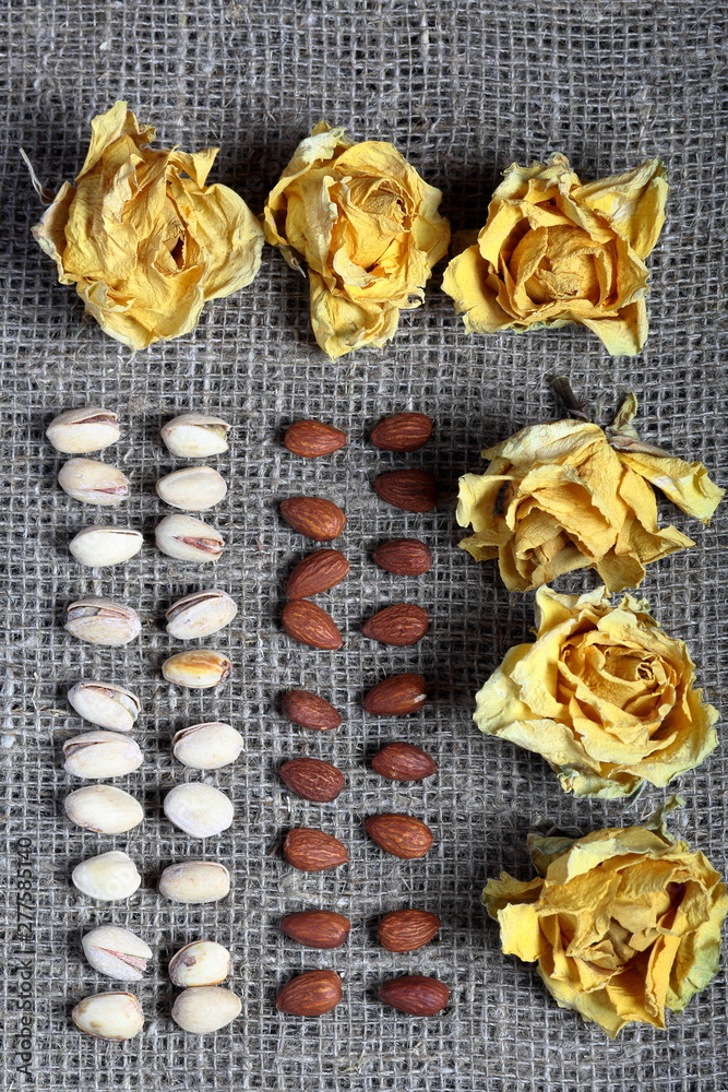 Pistachios and almonds are laid out in rows on coarse linen fabric. Decorated with dried flowers of yellow roses.