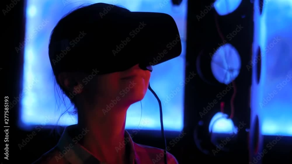 Woman using virtual reality headset and looking around at interactive technology exhibition with changing multi color light illumination. VR, augmented reality, immersive and entertainment concept