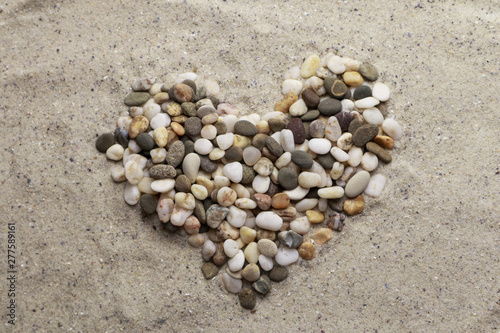 Heart made with pebbles on sand background