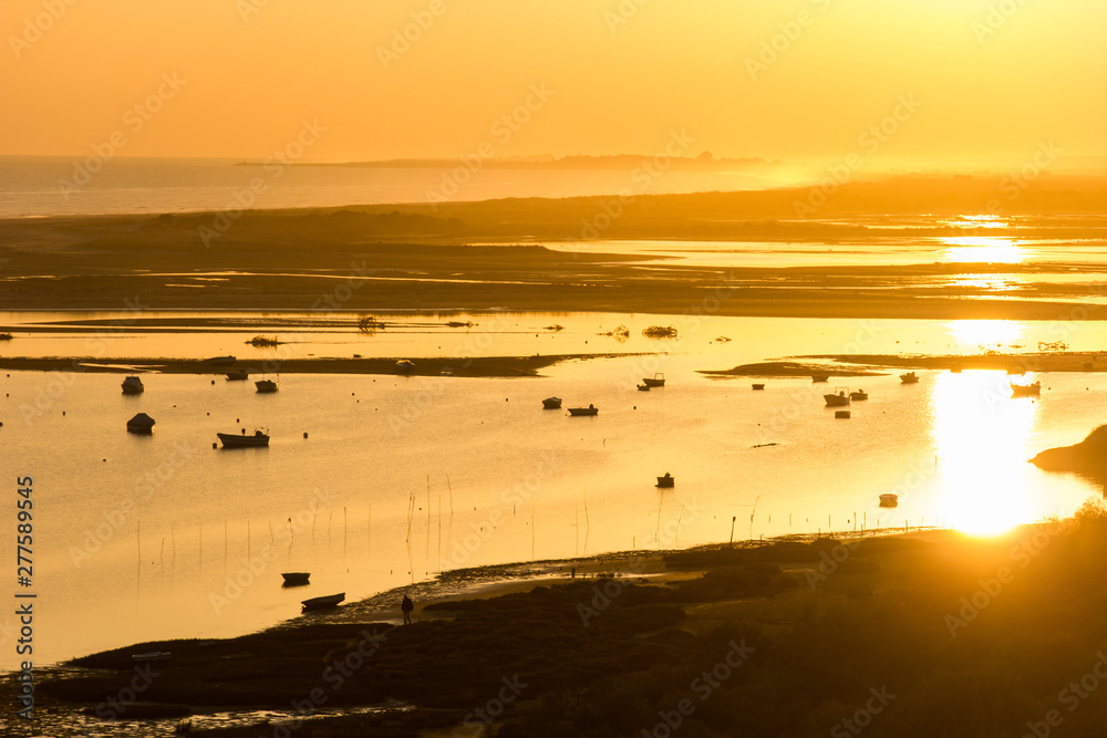 Sunset view of ocean and silhouette of boats in Ria Formosa near Faro, Portugal.