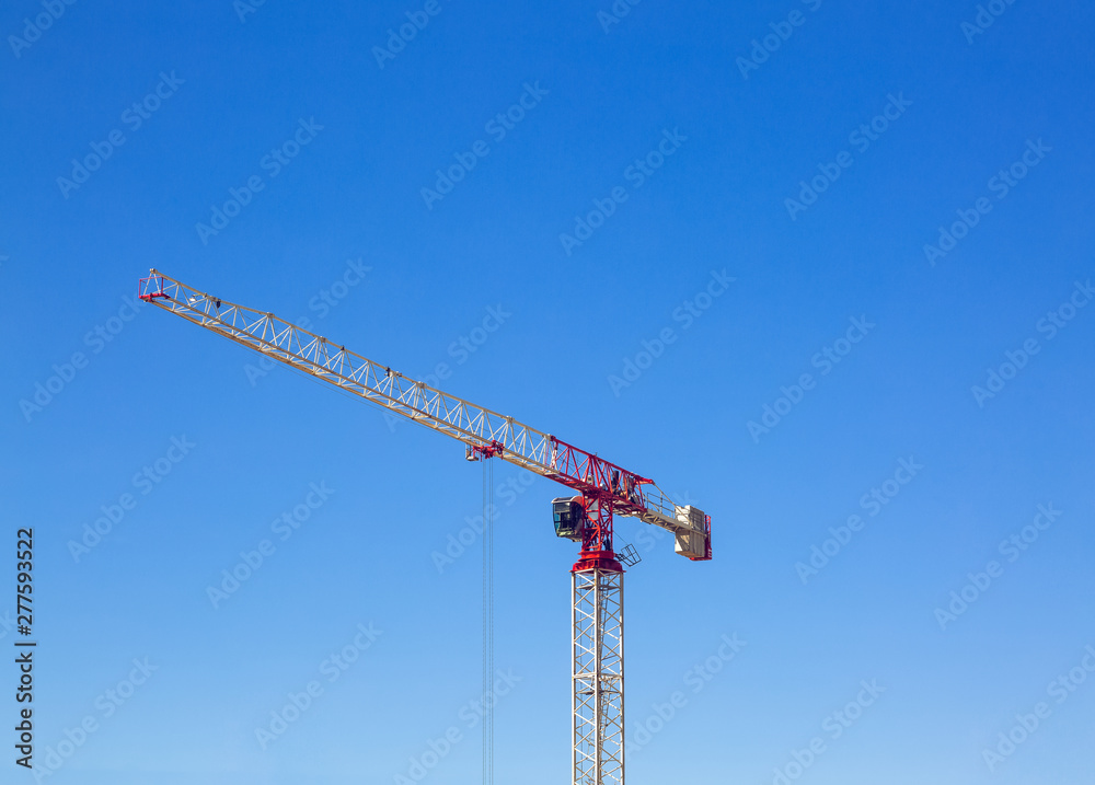 Industrial construction crane or column-jib crane with cabin works on the construction site and blue sky is a background. Space for your text. Industrial construction crane or column-jib crane with cabin works on the construction site and blue sky is a background. Space for your text.