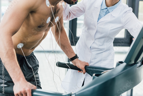 cropped view of doctor putting electrodes on shirtless sportsman during endurance test photo