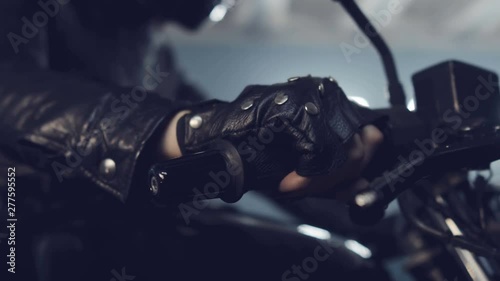 Brutal biker girl sits on a black motorcycle and turns the speed knob. Preparing for night races. Moto service. Frame for the film.