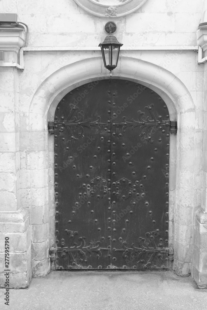 Medieval door black and white image on old stone house facade. Arched entrance and doorway to building front with simple door and old lantern outside 