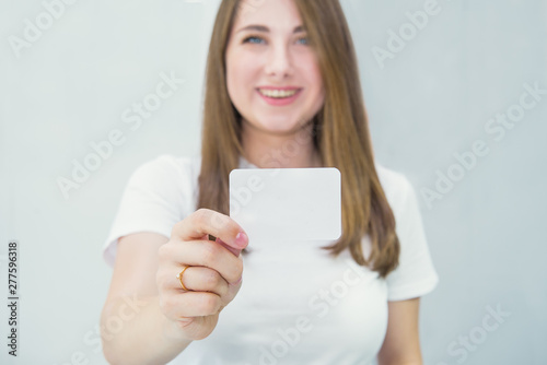 Business card or gift card. Blurred Happy and excited caucasian woman in casual clothes showing focused blank empty paper card with copy space for your design on light indoor background. © okrasiuk