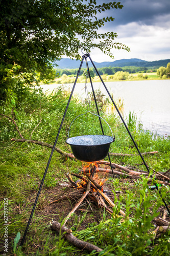 Cooking outdoor on a fire in a pot. Preparing goulash in a nature by the lake.