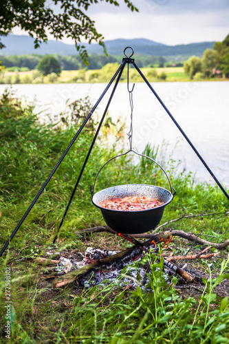 Cooking outdoor on a fire in a pot. Preparing goulash in a nature by the lake.