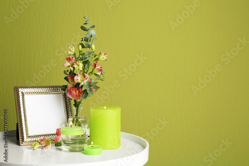Composition with burning candles, photo frame and fresh flowers on table near green wall. Space for text