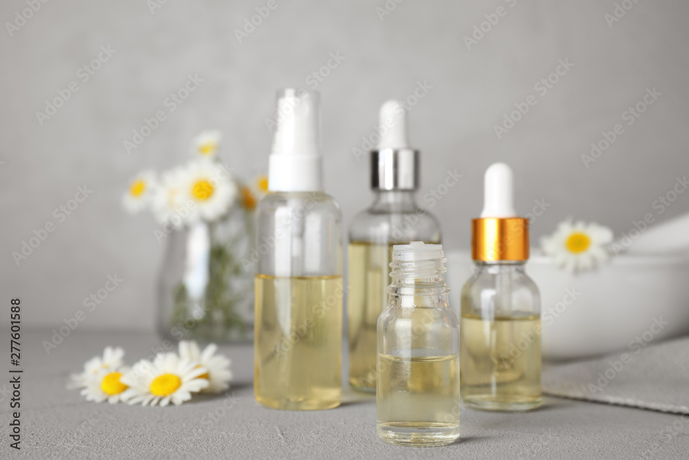 Bottles of chamomile essential oil and flowers on grey table, space for text Bottles of chamomile essential oil and flowers on grey table, space for text