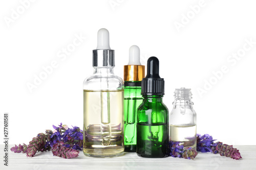 Bottles of sage essential oil and flowers on wooden table, white background